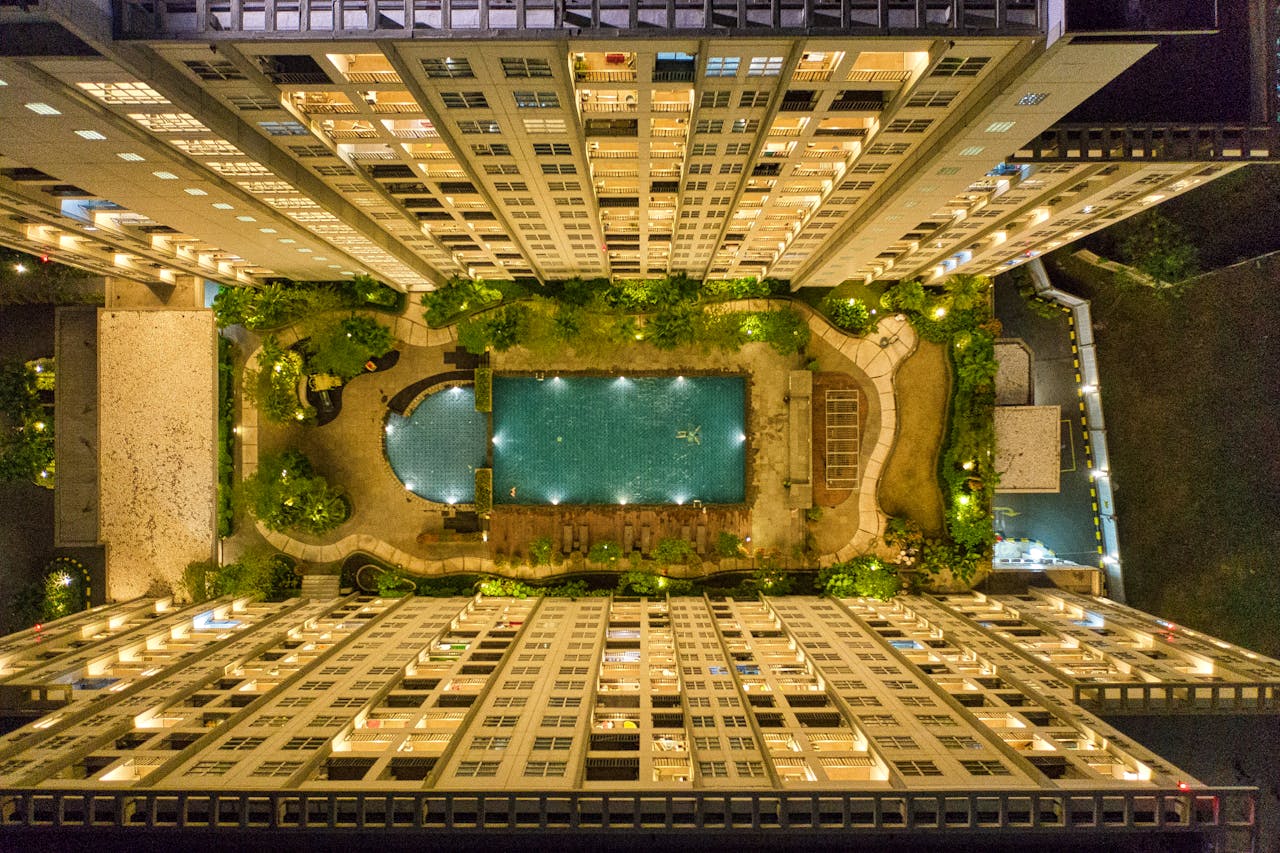 Captivating aerial view of illuminated modern urban buildings surrounding a swimming pool at night.